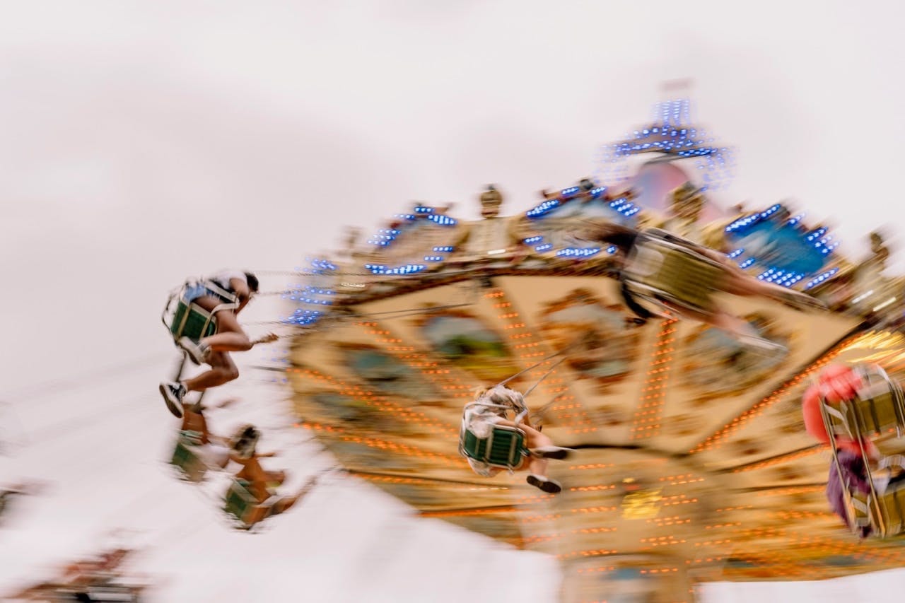 Motion-blurred fairground swing carousel spinning against a pale sky