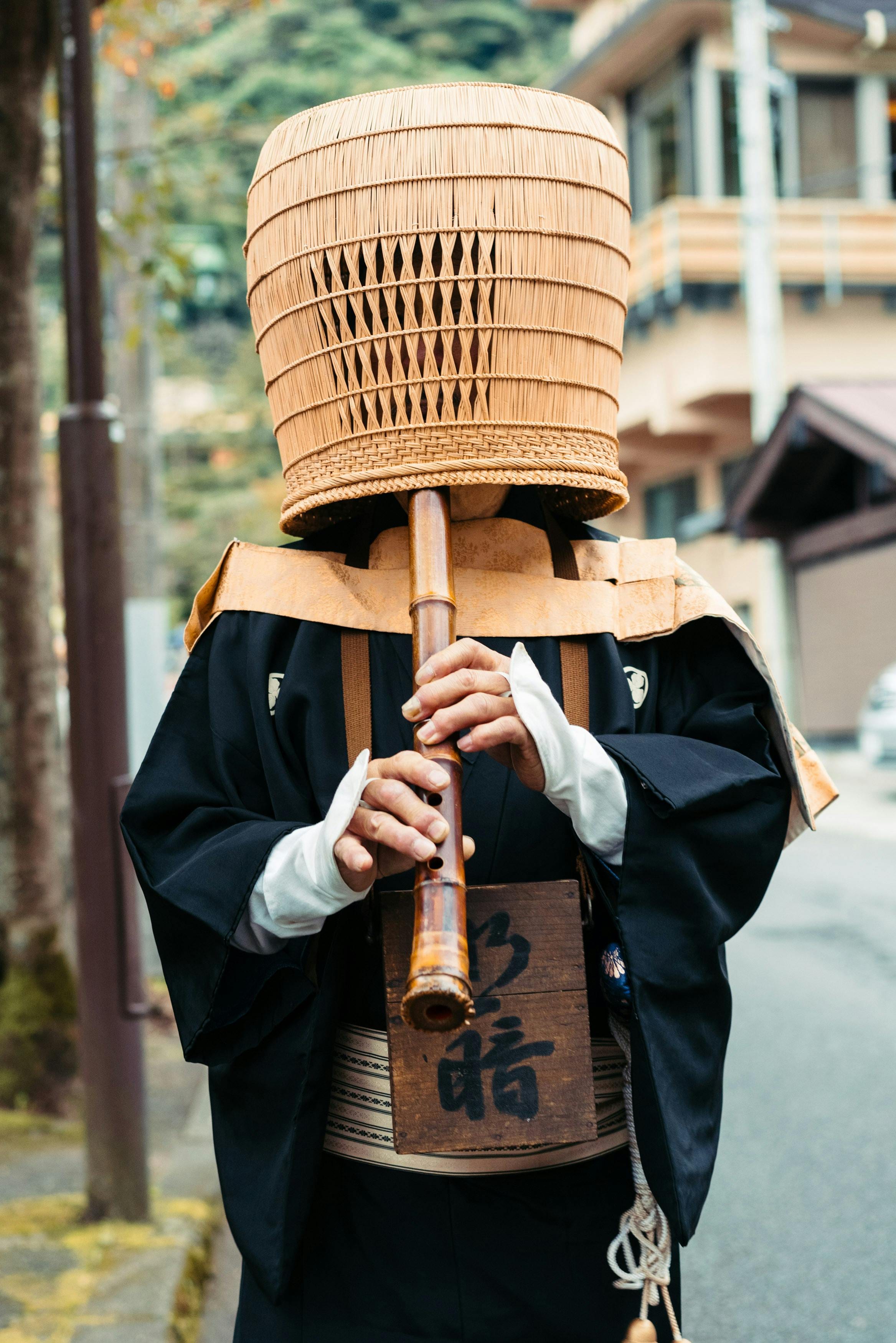 Komuso monk in a woven basket hat playing a bamboo shakuhachi flute on a street