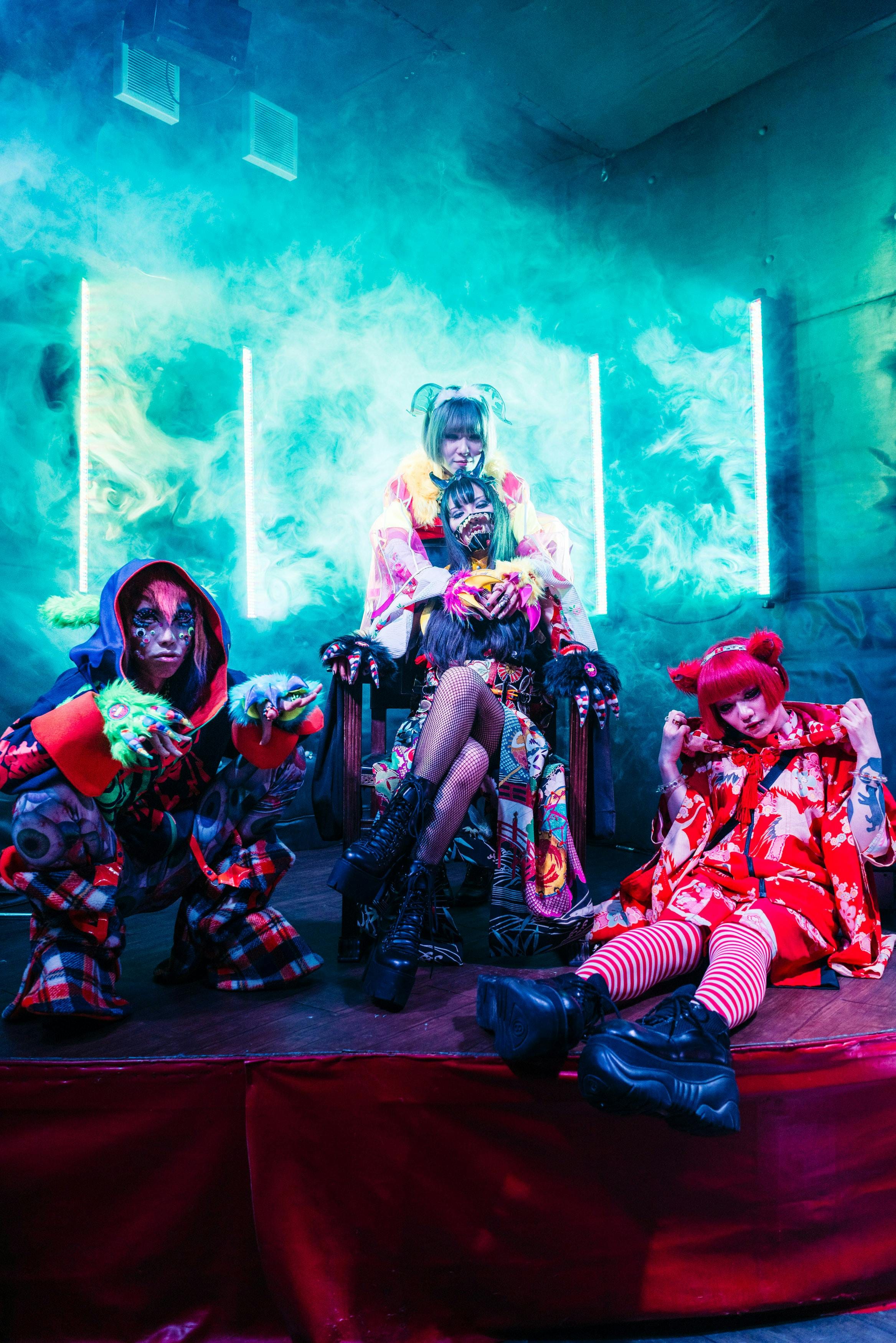 Four performers in bold Japanese street fashion amid teal neon and haze