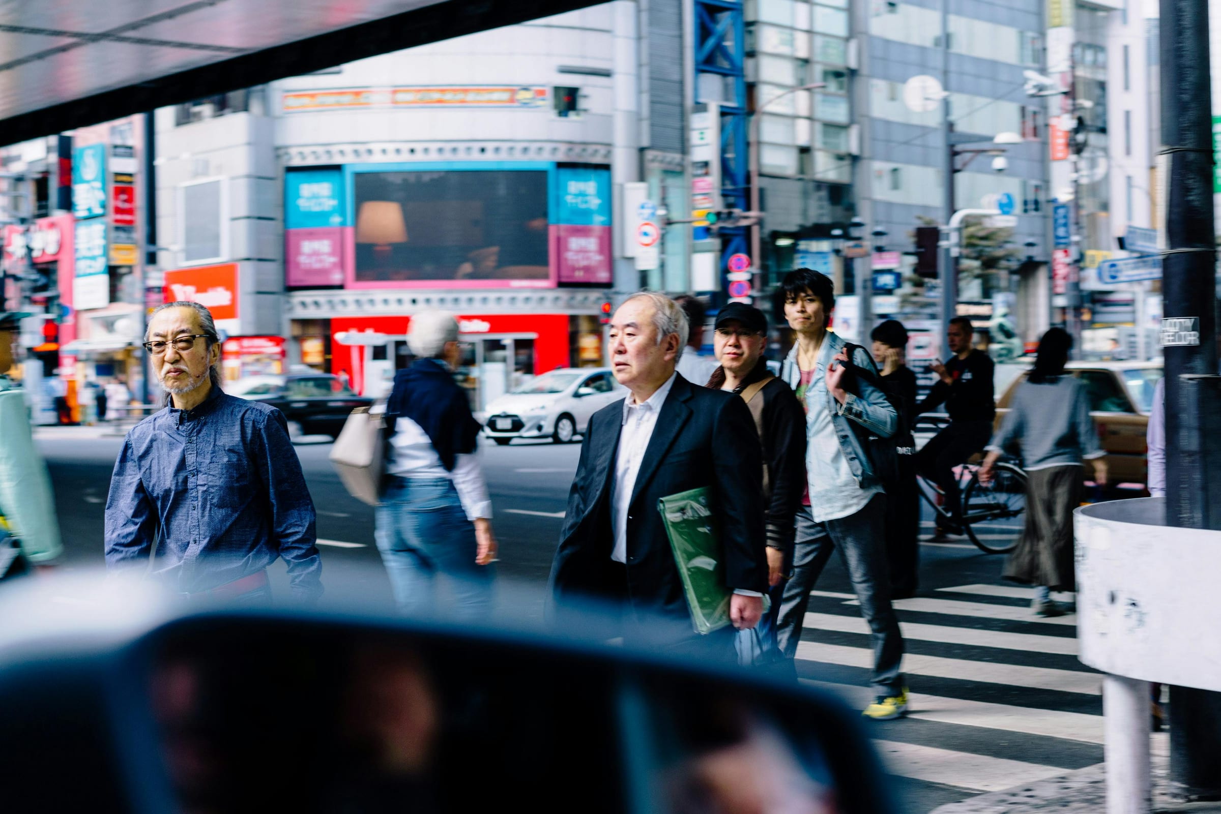 Pedestrians crossing a busy Tokyo intersection, seen through a car window