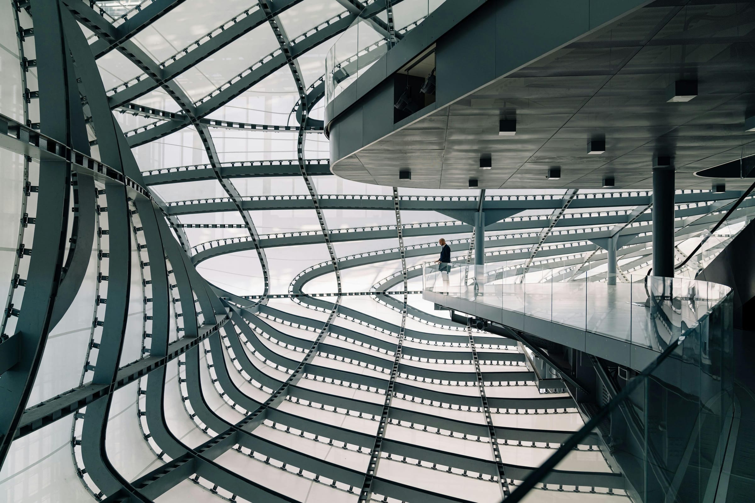 Lone suited figure on a walkway inside a soaring curved-steel Rome interior
