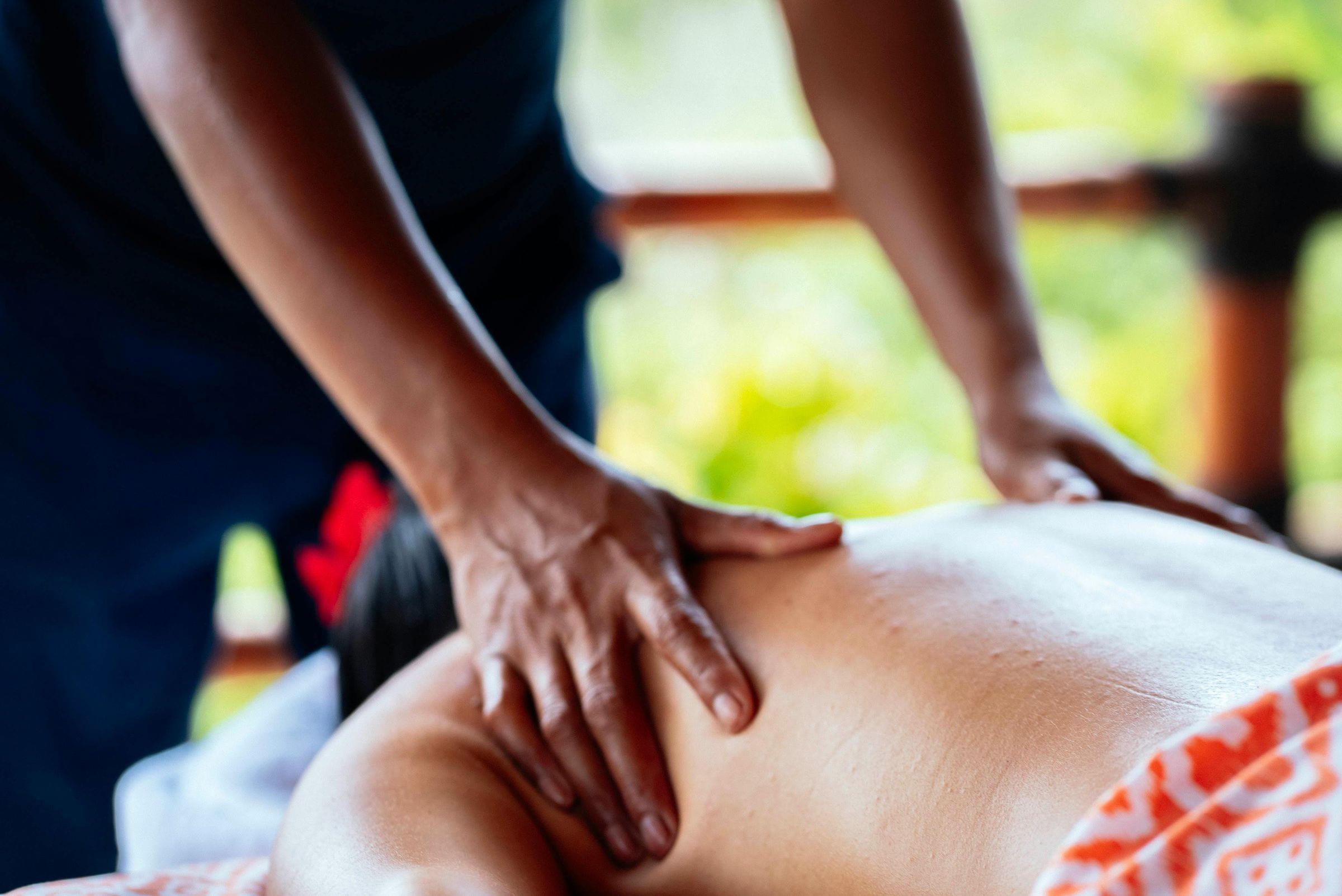 Spa therapist's hands working a guest's back before a jungle-green open window