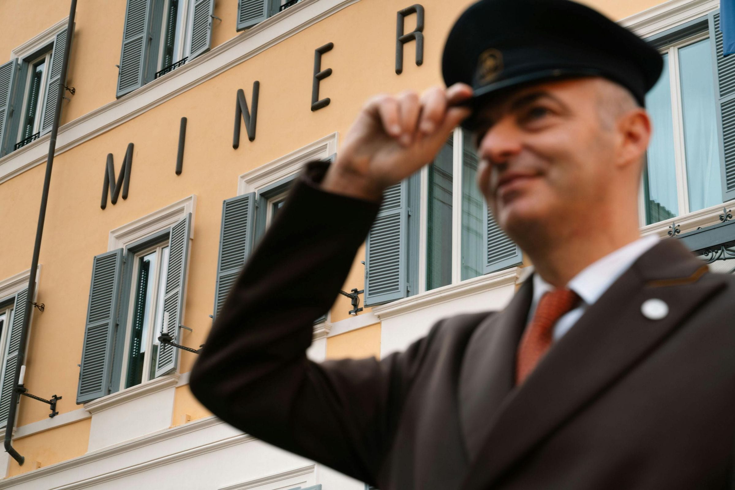 Uniformed doorman tipping his cap before the Minerva hotel facade in Rome
