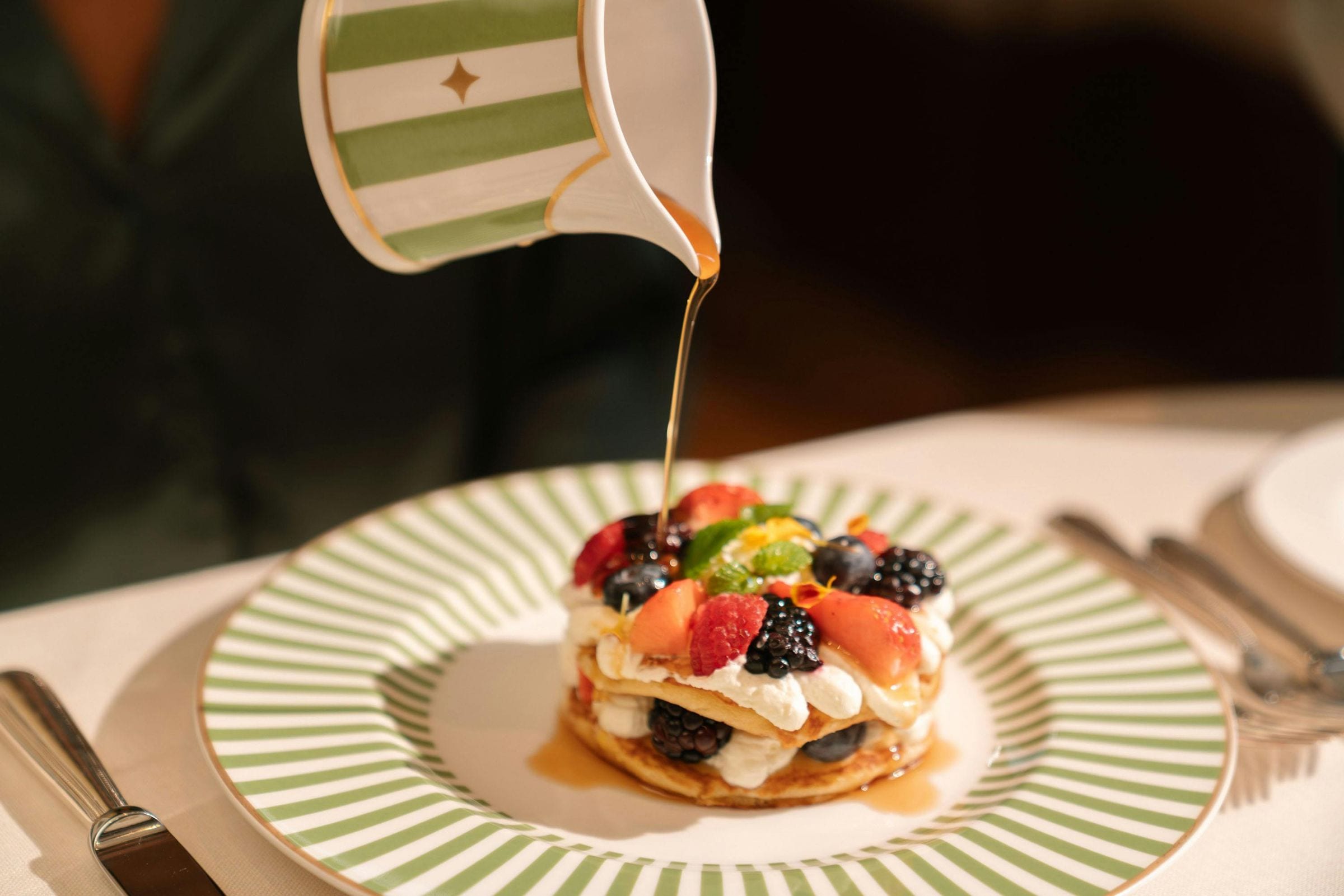 Caramel syrup poured over a berry-topped pancake stack on a green-striped plate