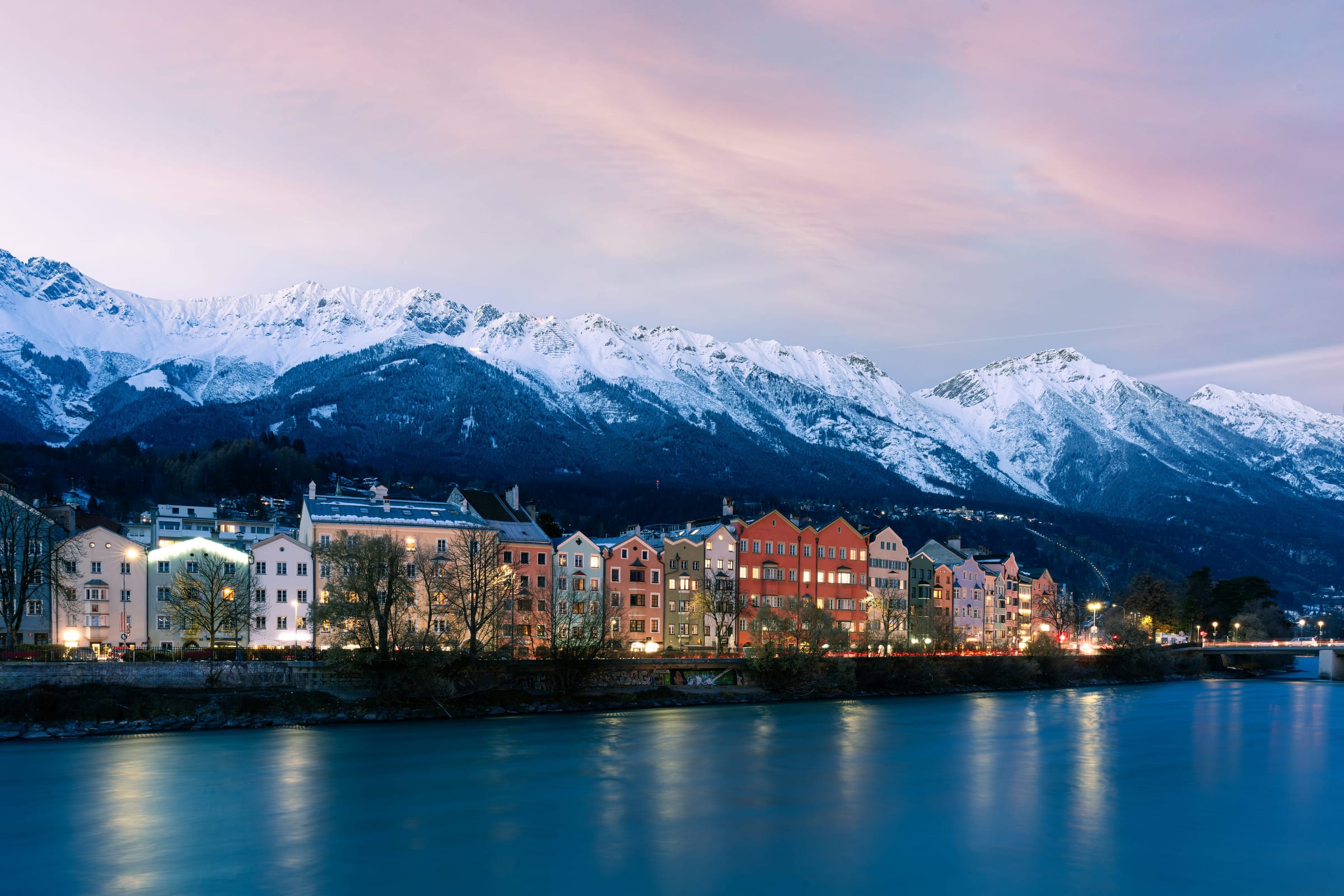 The painted houses of Innsbruck glowing at dusk along the river Inn beneath the snow-covered Nordkette range