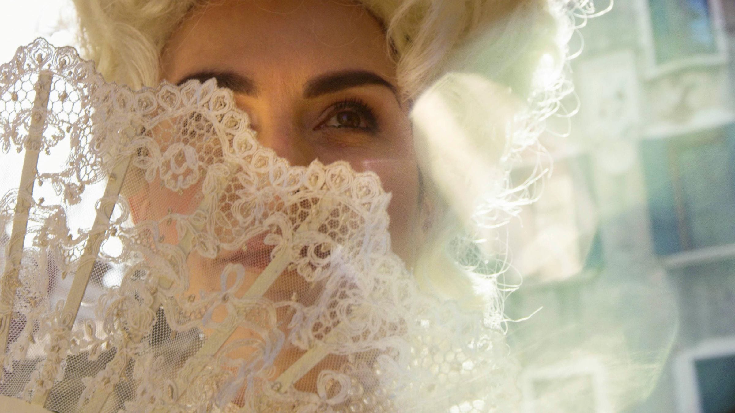 Close-up of a masked woman's eyes above a white lace fan, Venice Carnival