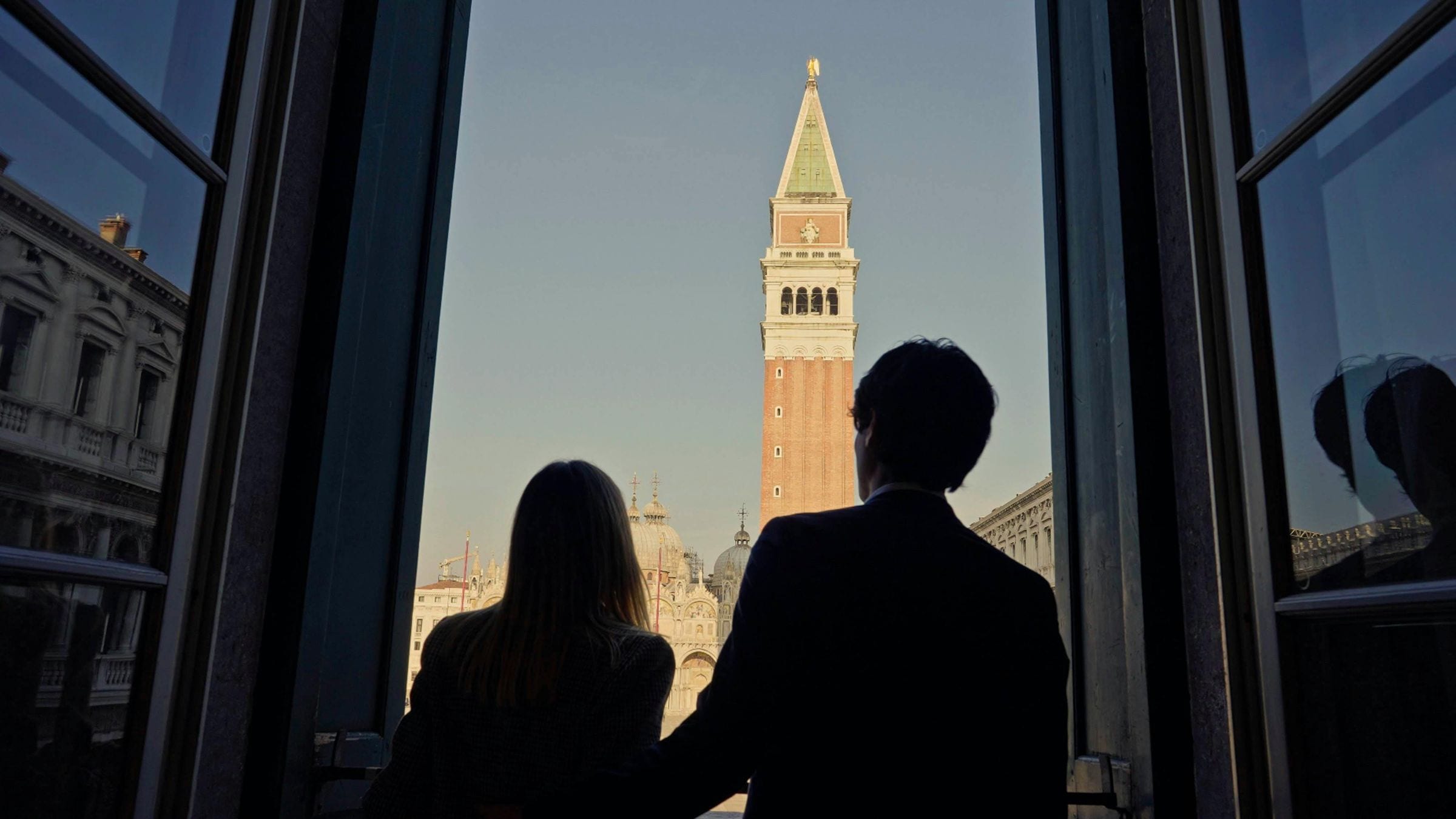 Silhouetted couple at a window facing St Mark's Campanile in warm morning light