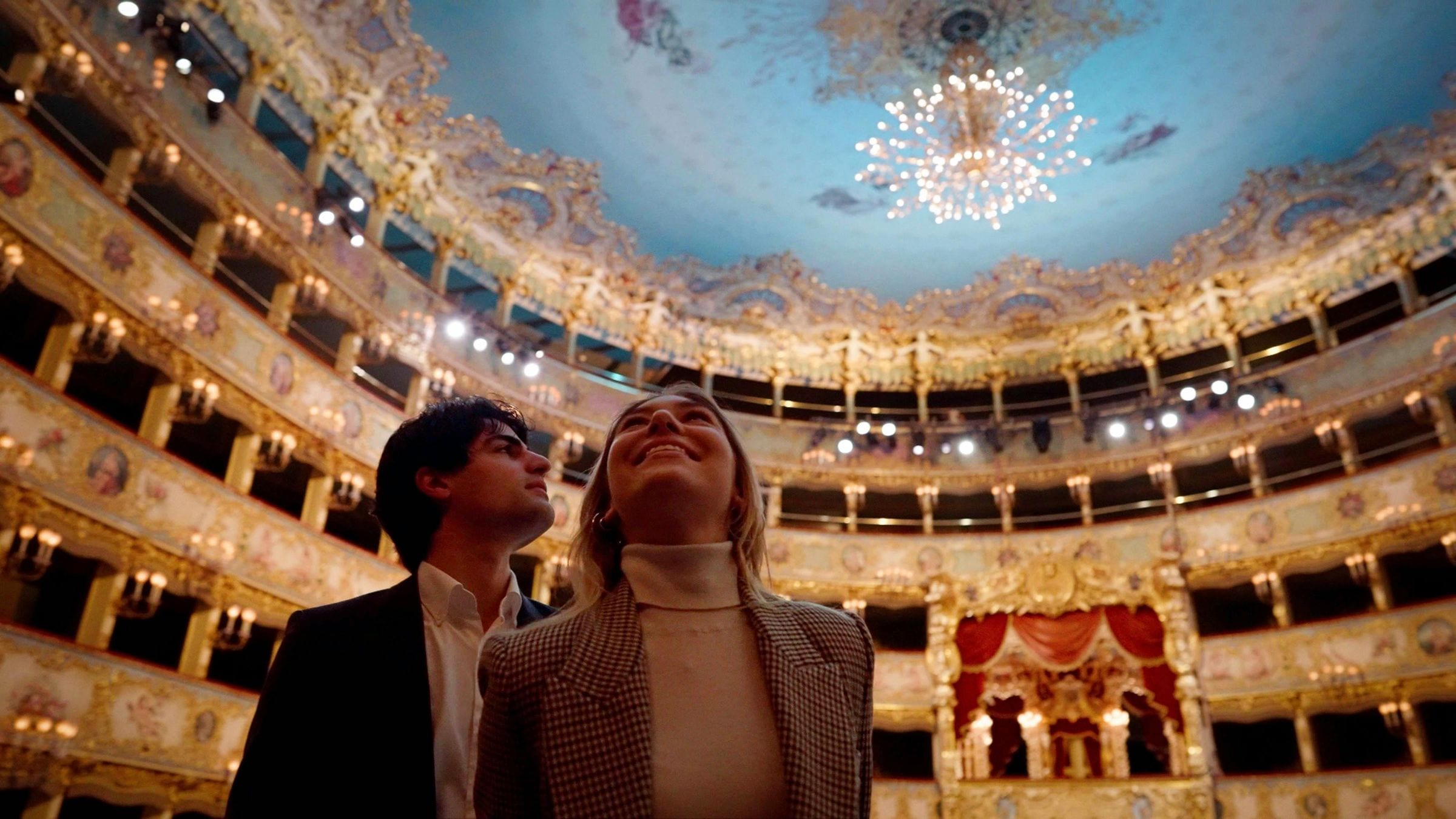 Couple gazing up at the frescoed ceiling and chandelier of La Fenice opera house