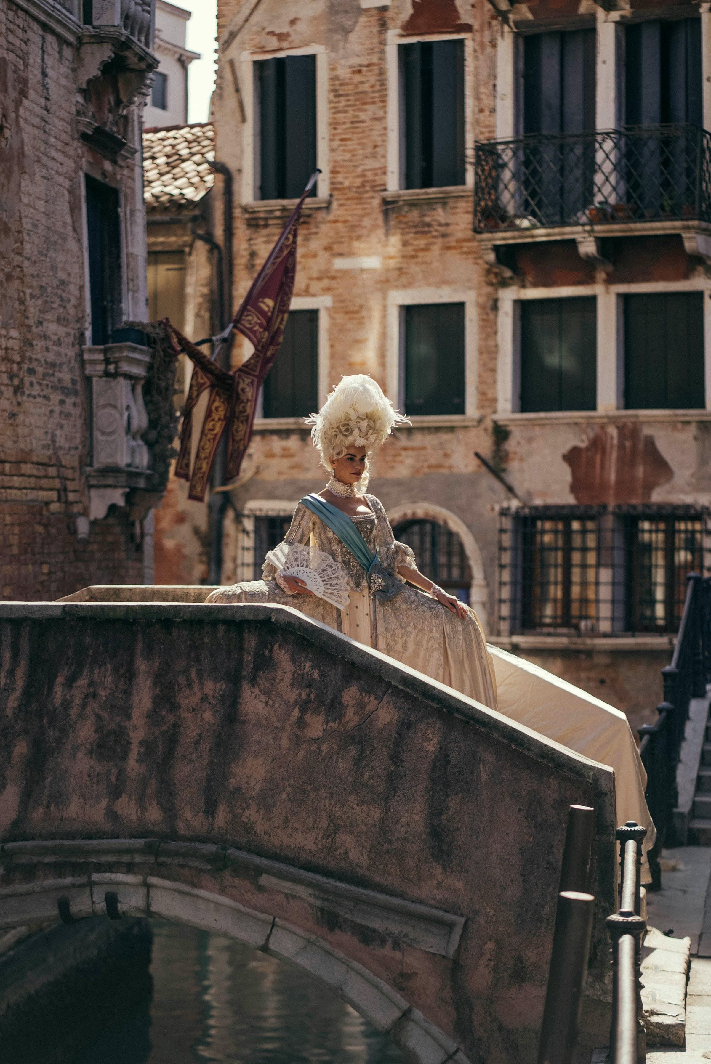 Woman in eighteenth-century Carnival costume and feathered wig posing on a Venice canal bridge