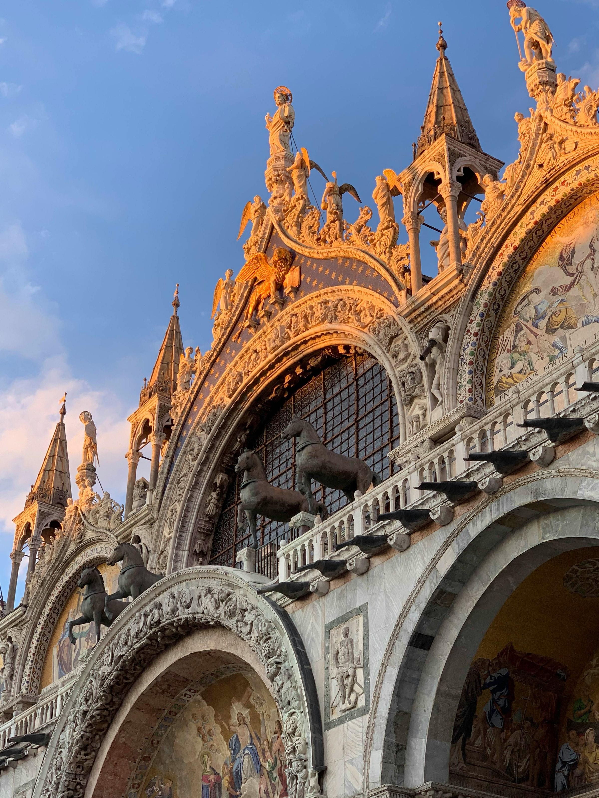 Golden-hour detail of St Mark's Basilica facade with gilded winged lion and spires