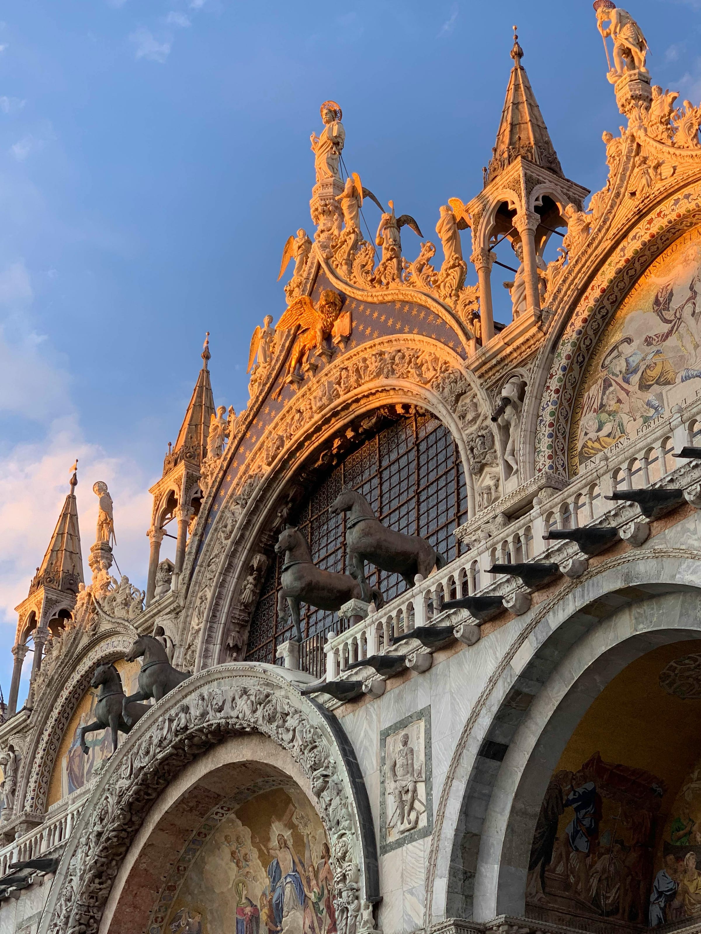 Golden-hour detail of St Mark's Basilica facade with gilded winged lion and spires