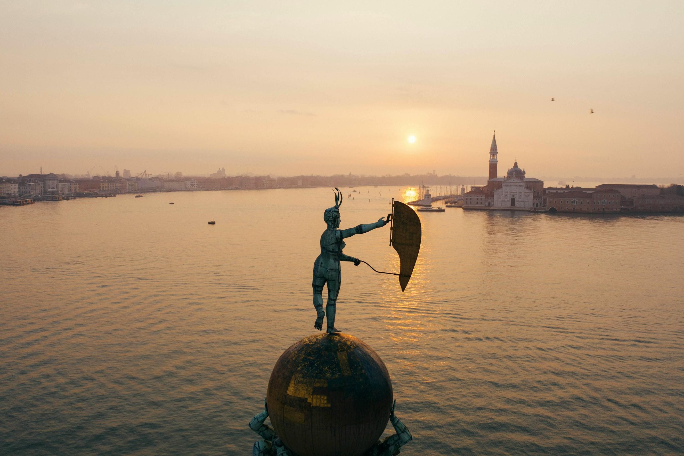 Bronze weathervane figure atop Punta della Dogana at sunrise, San Giorgio Maggiore beyond
